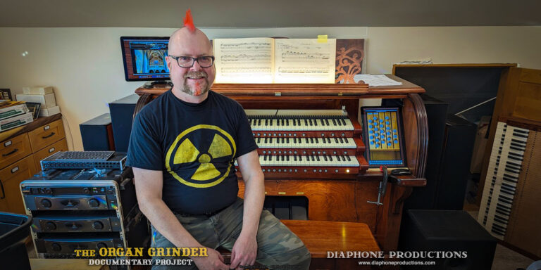 Photo of the filmmaker, a man with a red Mohawk, wearing a black T-shirt with a yellow "radiation symbol" graphic. He is sitting on an organ bench in front of a 3-manual console outfitted with multiple touch screens running virtual pipe organ software.